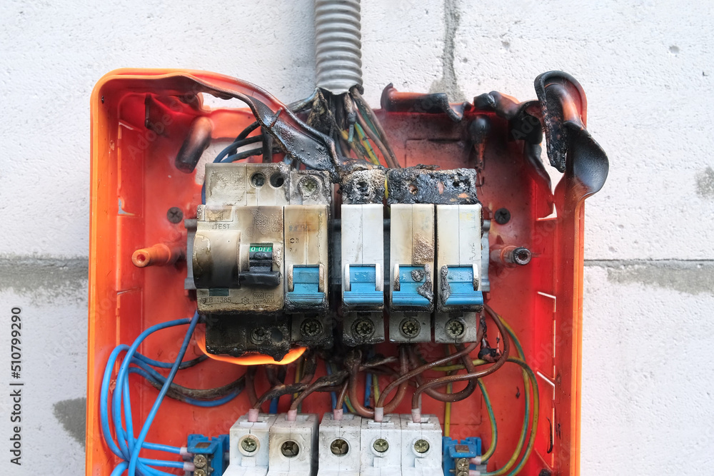 Burnt switchboard from overload or short circuit. Circuit breakers on fire  and smoke from overheating due to poor connection. Dangerous home  electrical wiring concept, close up view, selective focus Stock Photo