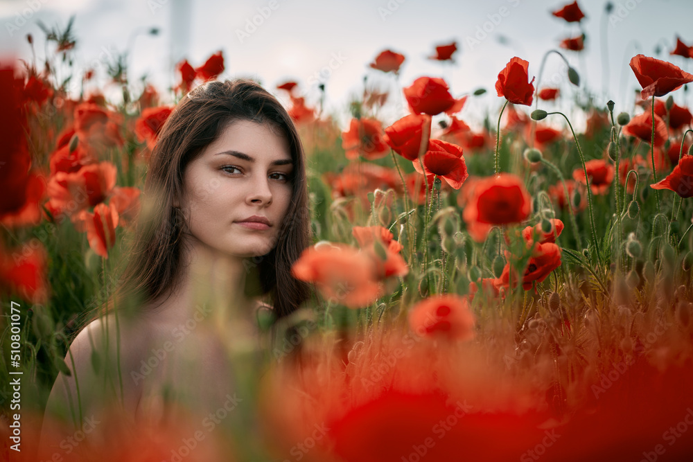 Beautiful young girl in the red poppy field. Brunette woman with naked shoulders outdoors. Concept of women's relaxation and happiness in the rural nature Beautiful young girl in the red poppy field. Brunette woman with naked shoulders outdoors. Concept of women's relaxation and happiness in the rural nature
