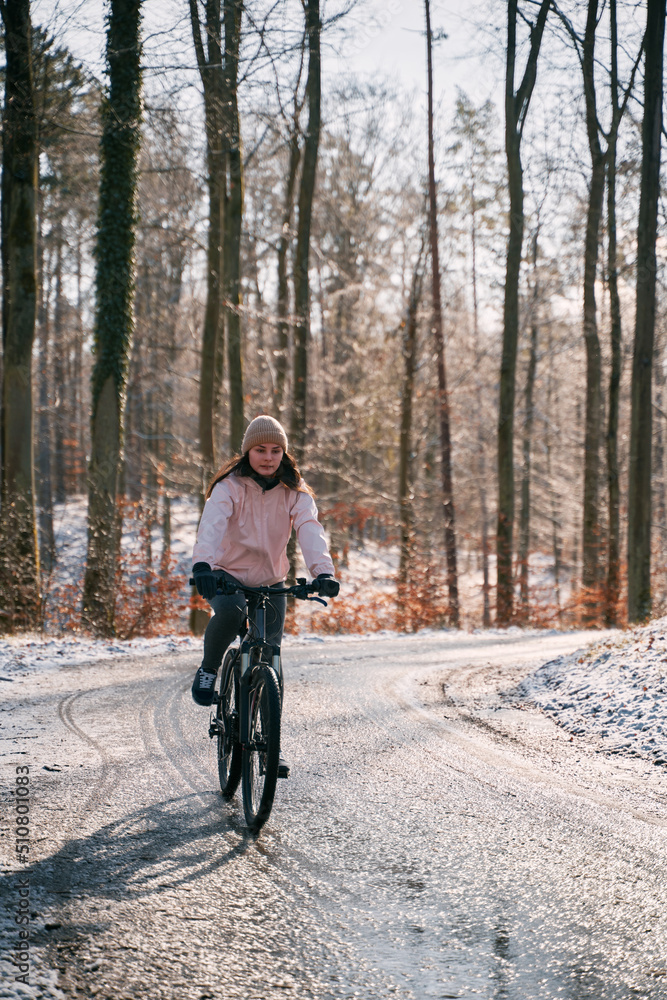 Obraz premium A woman rides a bike in winter. Concept of cycling during snowy weather. Snow and sun weather in the park