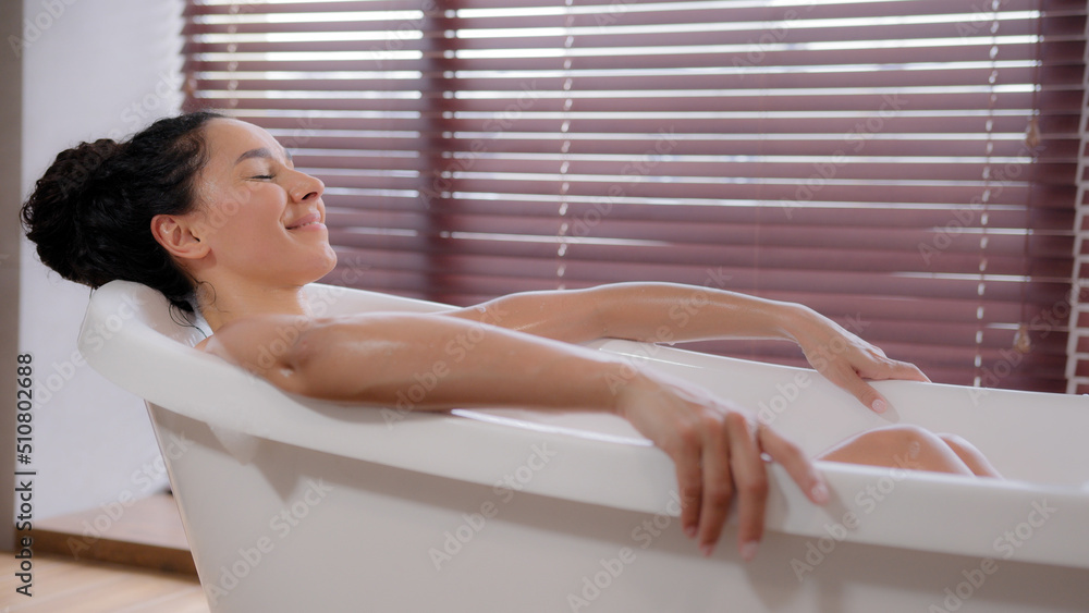 Young happy hispanic woman lying in hot bathtub resting comfortably with closed eyes feels pleasure smiling relaxing enjoying recreation in free time in bathroom bathing cleanses body routine hygiene Young happy hispanic woman lying in hot bathtub resting comfortably with closed eyes feels pleasure smiling relaxing enjoying recreation in free time in bathroom bathing cleanses body routine hygiene