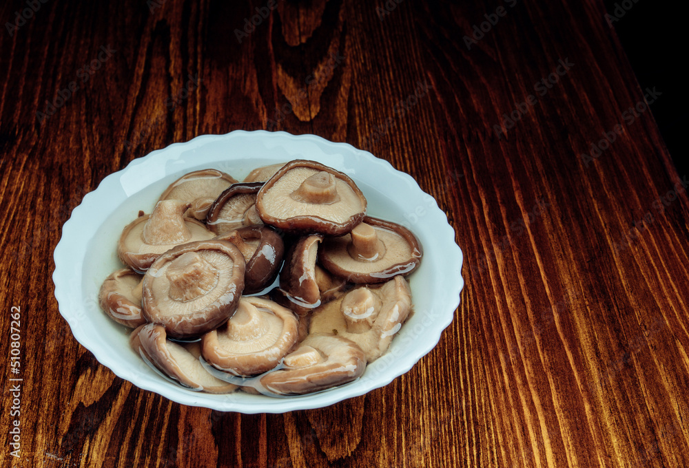 A white plate with pickled mushrooms stands on a wooden table . Healthy village food .