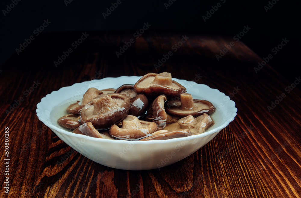 A white plate with pickled mushrooms stands on a wooden table side view . Healthy village food .