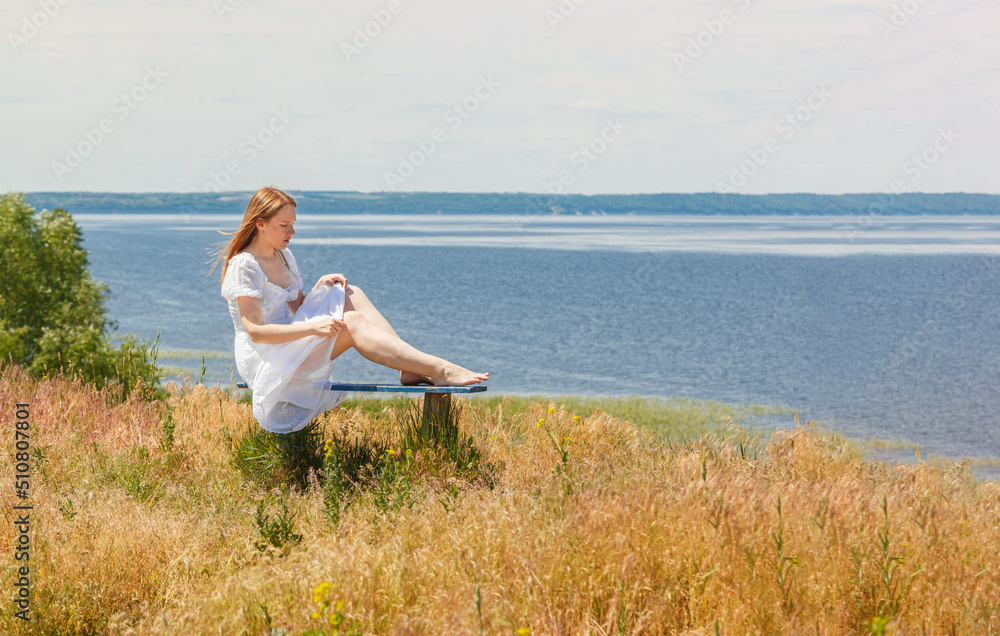 A beautiful girl sits on benches on the seashore with a view of the sky
