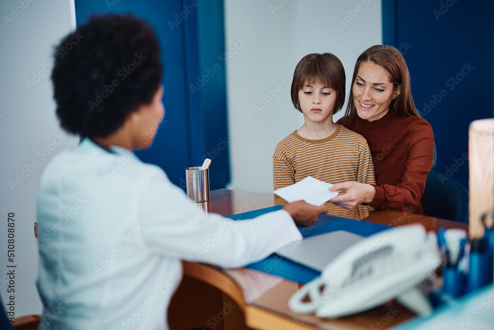 Obraz premium Happy mother receives prescription from pediatrician after son's medical exam at doctor's office.
