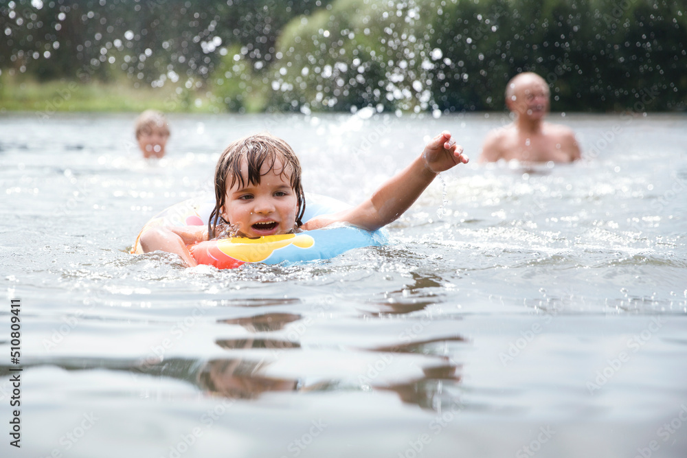 the little girl with colorful inflatable ring smiles as she plays in the river. Happy family plays in river. Family on vacation splashing in a lake. Happy grandparents enjoying summer vacation the little girl with colorful inflatable ring smiles as she plays in the river. Happy family plays in river. Family on vacation splashing in a lake. Happy grandparents enjoying summer vacation