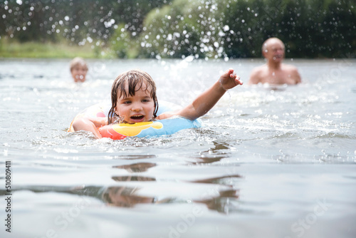 the little girl with colorful inflatable ring smiles as she plays in the river. Happy family plays in river. Family on vacation splashing in a lake. Happy grandparents enjoying summer vacation