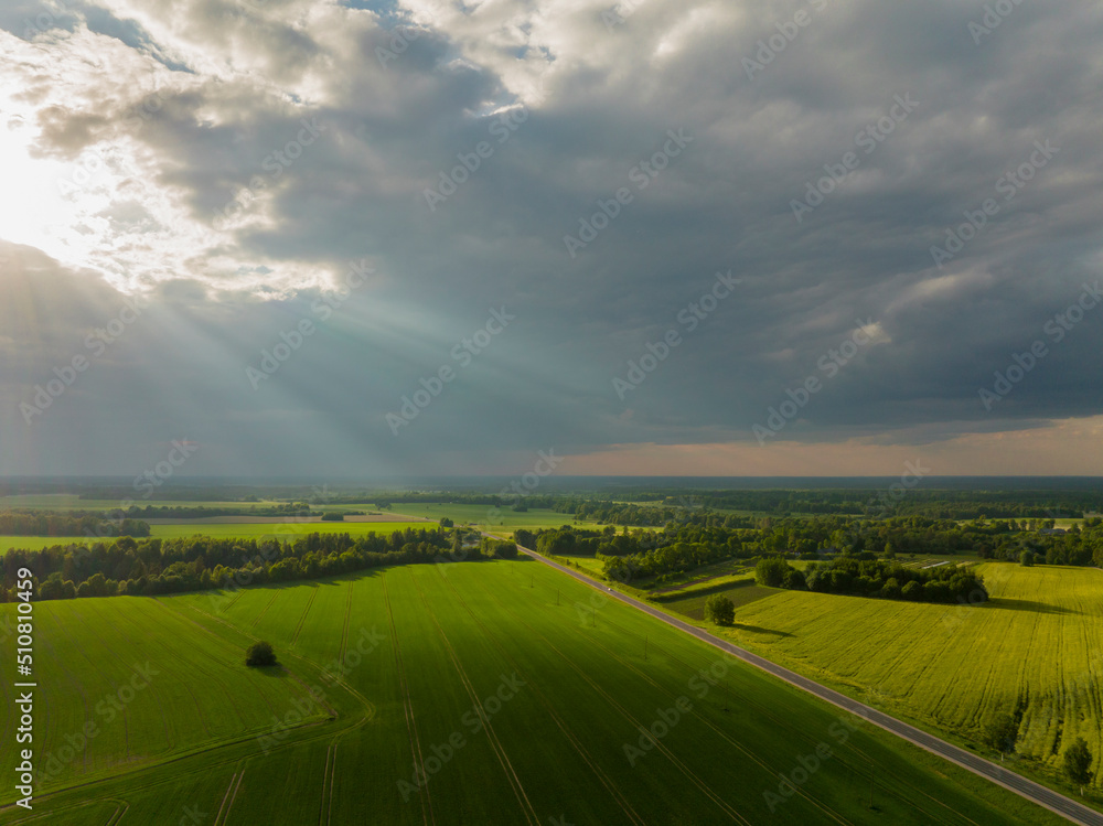 The sun's rays pass through the clouds, the earth's path divides the green fields