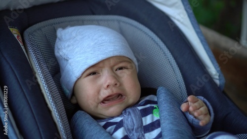 A newborn baby is crying while lying in a stroller. The child is unwell.