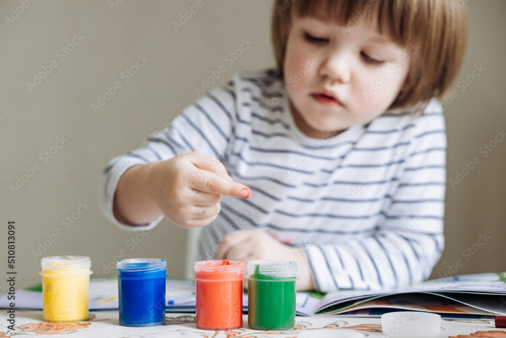 Finger painting. Portrait of cute little boy painting with fingers at home. Close-up of child's hand in colorful paints. Early education concept. Sensory play. Development of fine motor skills. Finger painting. Portrait of cute little boy painting with fingers at home. Close-up of child's hand in colorful paints. Early education concept. Sensory play. Development of fine motor skills.