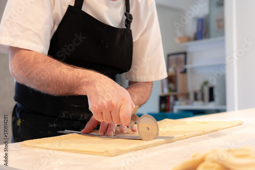 Detail of the hands of a man cooking croissants, measuring the puff pastry and making cuts, work at home