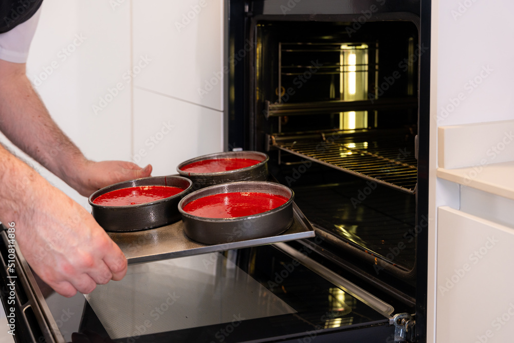 Hands of a man cooking a red velvet cake at home, putting the red cake in the oven, work at home Hands of a man cooking a red velvet cake at home, putting the red cake in the oven, work at home