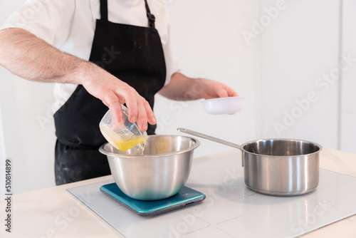 Fototapeta Naklejka Na Ścianę i Meble -  Hands of a man cooking a red velvet cake at home, preparing Swiss meringue with egg whites in a bain-marie, work at home