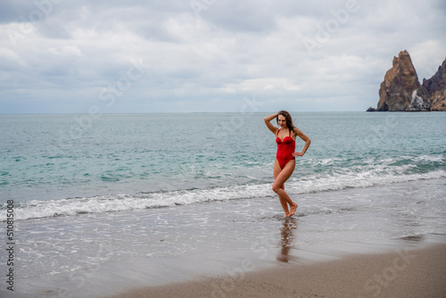 A beautiful and sexy brunette in a red swimsuit on a pebble beach, Running along the shore in the foam of the waves