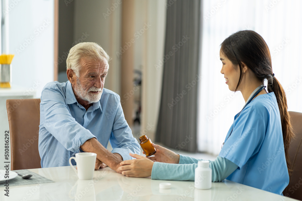 Obraz premium Caring Asian nurse giving medication and glass of water to senior old man patient at hospital. Friendly female doctor caring and giving medicine elderly man patient at nursing home.