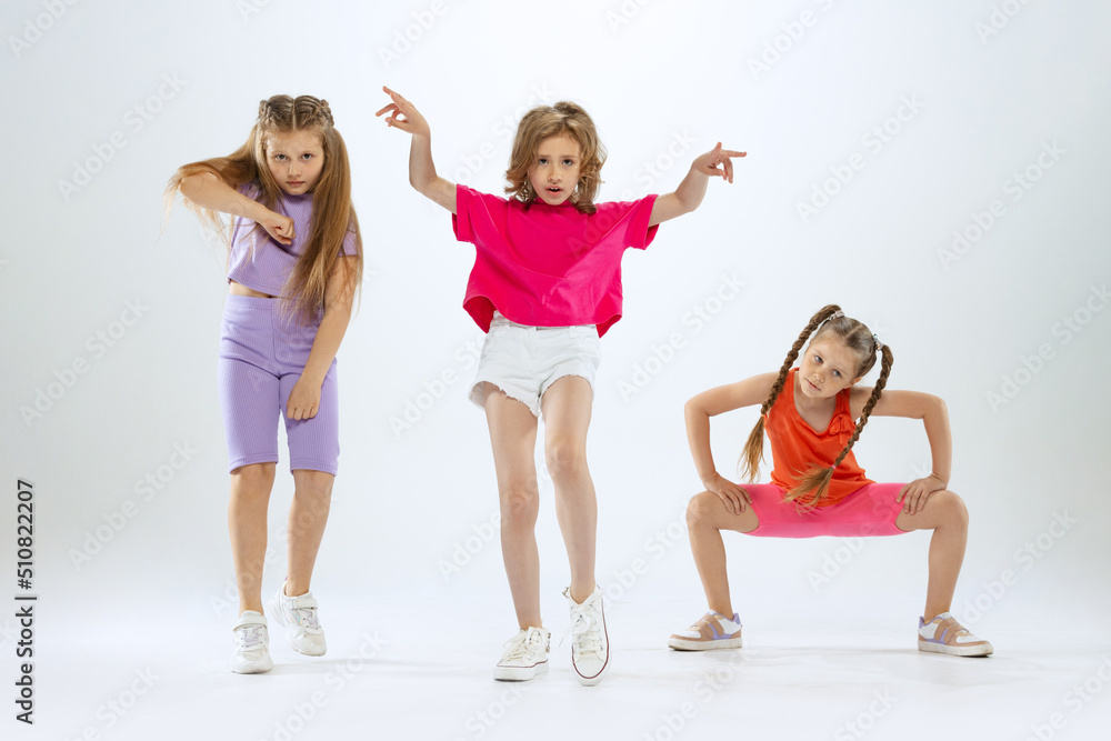 Portrait of happy, active little girls, happy kids in bright colorful clothes dancing isolated on white studio background. Concept of music, fashion, art, childhood, hobby Portrait of happy, active little girls, happy kids in bright colorful clothes dancing isolated on white studio background. Concept of music, fashion, art, childhood, hobby