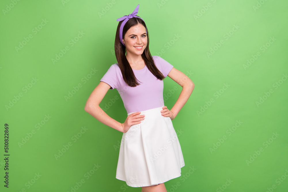 Photo of adorable charming woman wear violet t-shirt hairband arms waist isolated green color background Photo of adorable charming woman wear violet t-shirt hairband arms waist isolated green color background