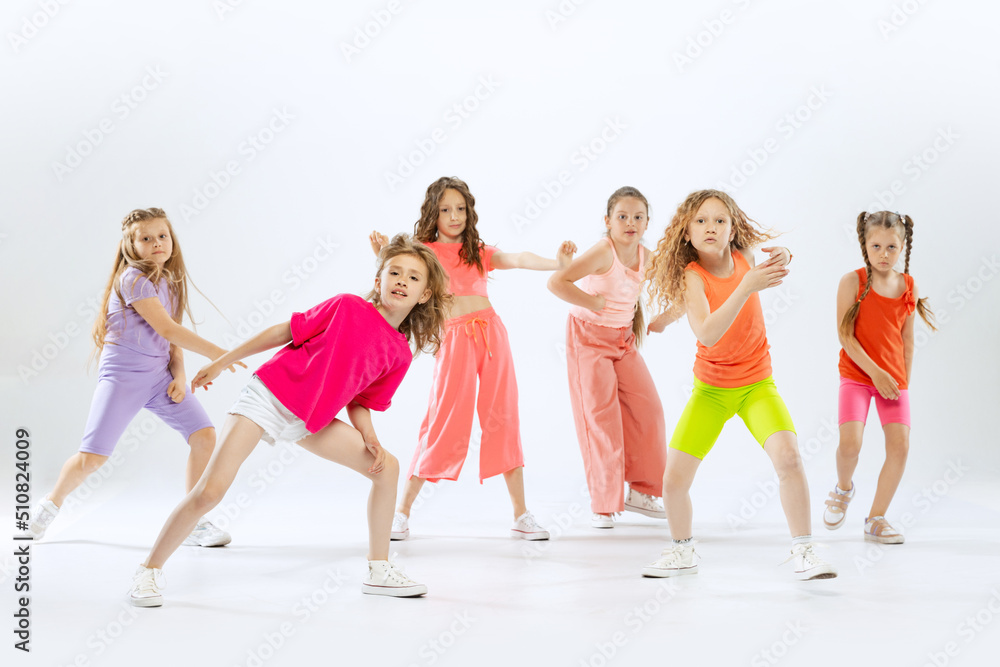 Obraz premium Happy, sportive little girls, kids in bright colorful clothes dancing modern dance isolated on white studio background. Concept of music, fashion, art, childhood, hobby