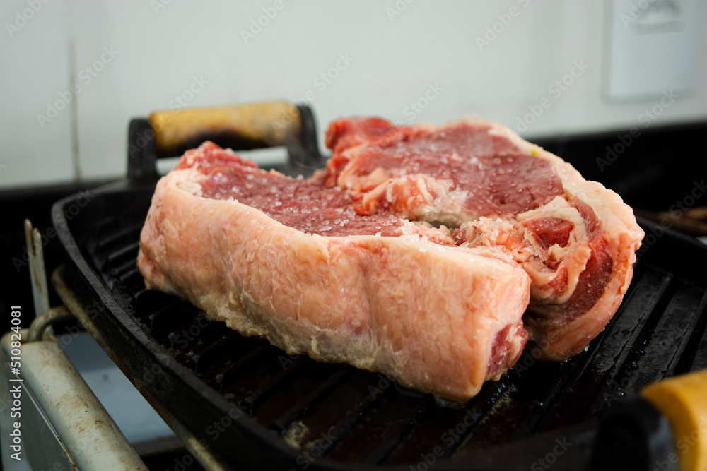 red raw sirloin steak being grilled on iron cast during day-time family lunch on a weekend