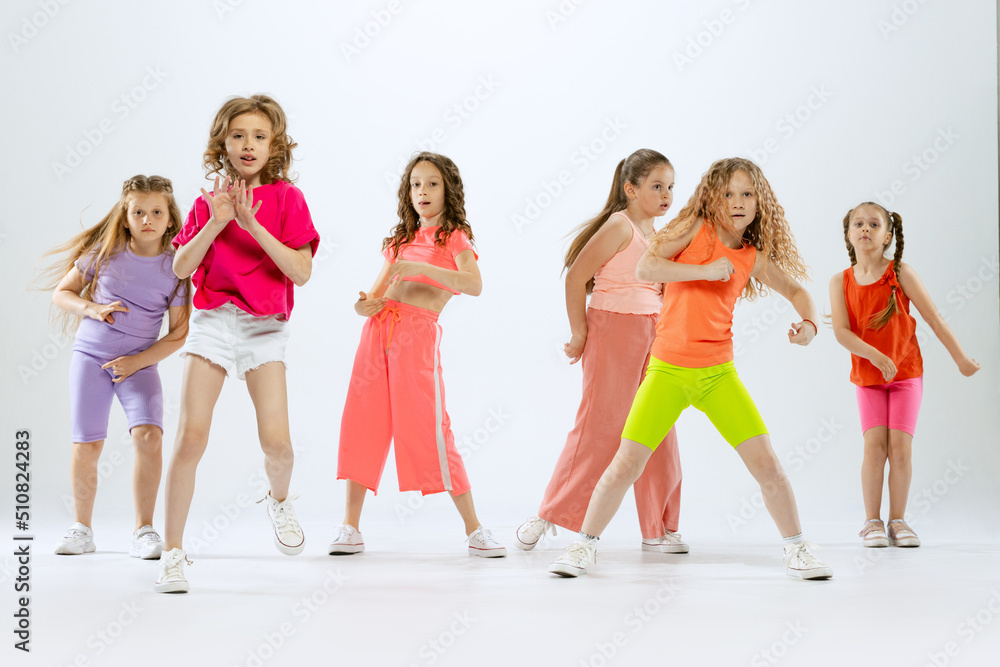 Portrait of happy, active little girls, happy kids in bright colorful clothes dancing isolated on white studio background. Concept of music, fashion, art, childhood, hobby Portrait of happy, active little girls, happy kids in bright colorful clothes dancing isolated on white studio background. Concept of music, fashion, art, childhood, hobby