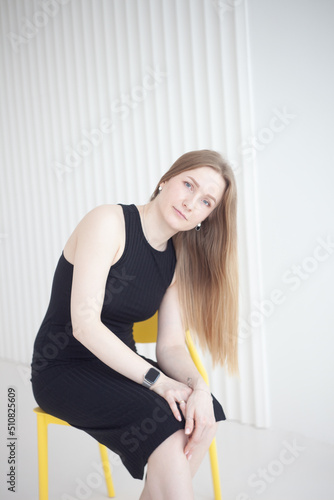 Girl in a black dress sits on a chair