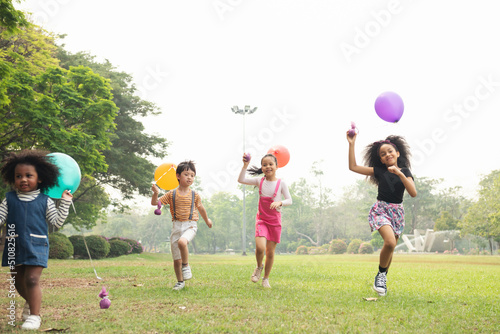 Group of kids running in the spring field at public park with balloon. Movement and blurry too soft. people children plying outdoors concept.