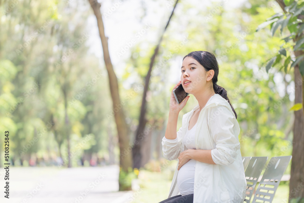 Happy pregnant woman sitting relax in the park and using a smartphone Happy pregnant woman sitting relax in the park and using a smartphone