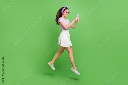 Full body photo of impressed brunette lady run look telephone wear head band glasses t-shirt skirt shoes isolated on green background © deagreez