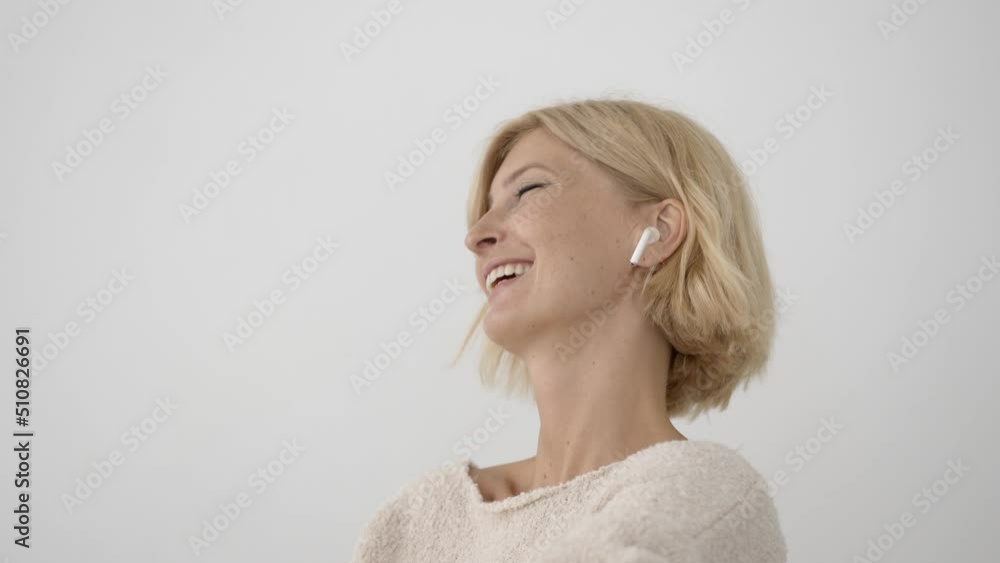 Attractive woman talking using wireless headphones, white wall background Attractive woman talking using wireless headphones, white wall background