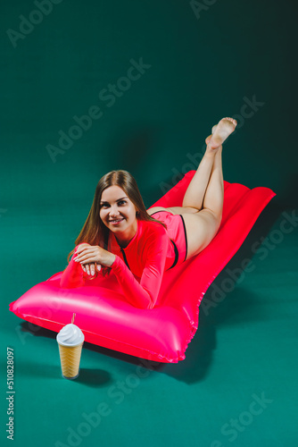 Attractive woman in pink one-piece swimsuit lies on inflatable mattress with cocktail isolated on green background. Summer vacation vacation at sea tanning concept