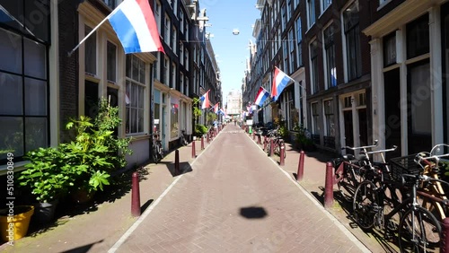 Beautiful street in Amsterdam, with Netherlands flags displayed on typical dutch buildings. Old centre district and typical architecture in Holland.