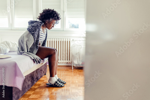 Unhealthy young woman with stomachache sitting on the bed at home. Young woman suffering from stomach cramps in her bedroom. Attractive young woman suffering from stomach cramps in her bedroom at home