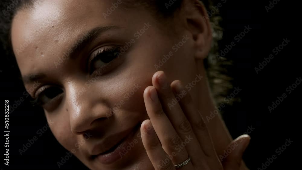 Young African American cute woman with dark curly hair strokes her face looking at the camera smiling on black background | Anti-acne concept Young African American cute woman with dark curly hair strokes her face looking at the camera smiling on black background | Anti-acne concept