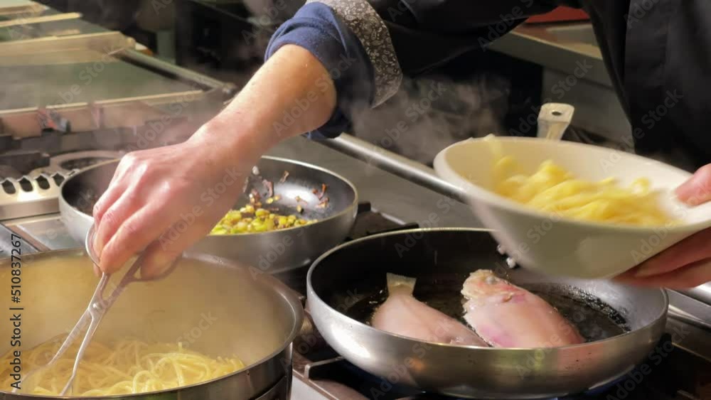 Chef serving spaghetti in a bowl for the staff meal, while he is frying red mullet for clients Chef serving spaghetti in a bowl for the staff meal, while he is frying red mullet for clients