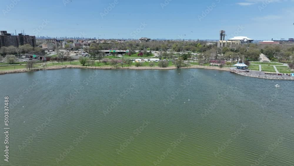 An aerial view high over Meadow Lake on a beautiful day in Queens, NY. There is a flock of birds flying over the water as the drone camera dolly in and tilt down over the birds in flight. An aerial view high over Meadow Lake on a beautiful day in Queens, NY. There is a flock of birds flying over the water as the drone camera dolly in and tilt down over the birds in flight.