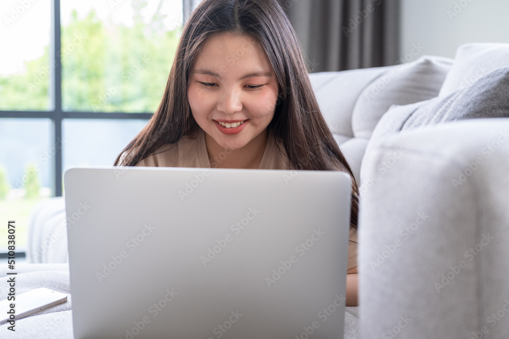 beautiful young asian woman in casual cozy clothes using laptop sitting on couch at modern apartment