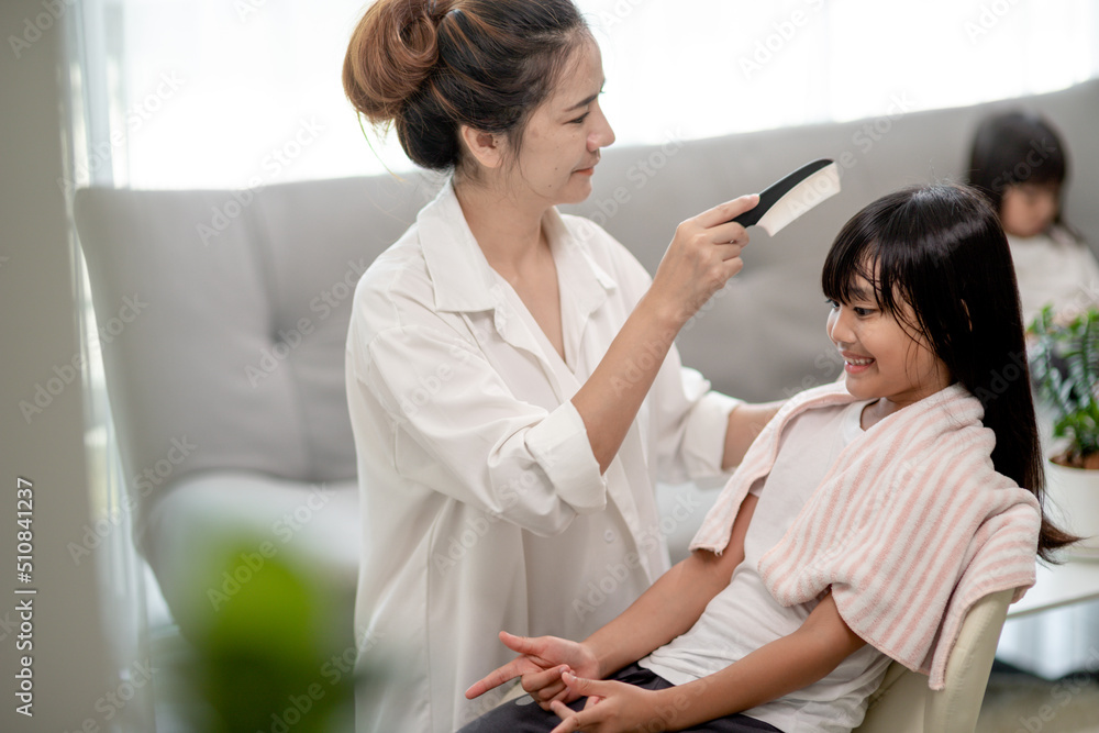 Asian Mother cutting hair to her daughter in living room at home while stay at home safe from Covid-19 Coronavirus during lockdown. Self-quarantine and social distancing concept. Asian Mother cutting hair to her daughter in living room at home while stay at home safe from Covid-19 Coronavirus during lockdown. Self-quarantine and social distancing concept.