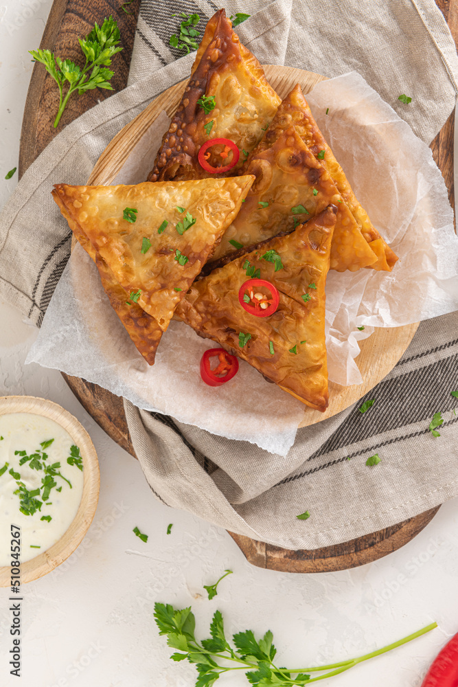 Indian samosas - fried or baked pastry with savoury filling, popular Indian snacks, served with yogurt sauce in areca leaf dishes with spices on kitchen countertop. Indian samosas - fried or baked pastry with savoury filling, popular Indian snacks, served with yogurt sauce in areca leaf dishes with spices on kitchen countertop.
