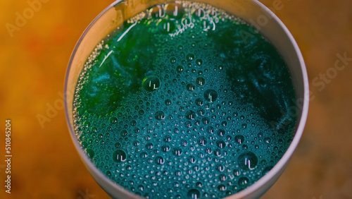 Close-up of beautiful sparkling drink in transparent glass. Stock footage. Luxurious colored drink with bursting bubbles on surface and iridescent sparkling texture