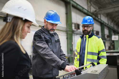 Manager supervisors and industrial worker in uniform doing control in large metal factory hall and talking.