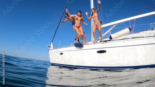 Group of friends diving in the water during a boat excursion, young people jumping inside ocean in summer vacation from a sail, having fun, luxury vacation lifestyle