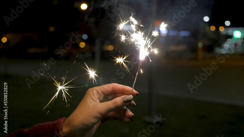 Close up of woman holding sparkler on the street. Closeup of Girl with Sparklers. Female hand holding sparklers in the street. Holiday concept