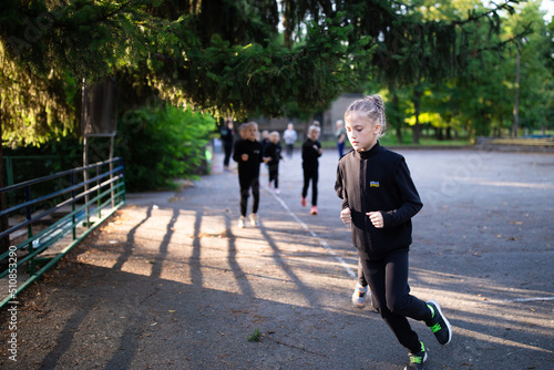 Girl running on rhythmic gymnastics training with other trainees outdoors in sports camp in summer