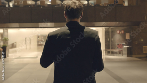 Rear view of businessman near the reception. Stock. There are glass wall offices. Rear view of businessman in hotel photo
