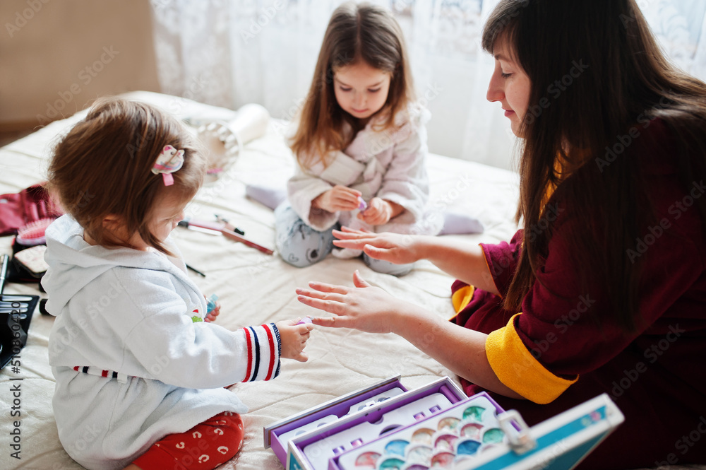 Mother and daughters doing manicures on the bed in the bedroom.