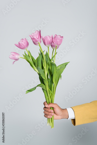 cropped view of african american man holding bouquet of pink tulips isolated on grey.