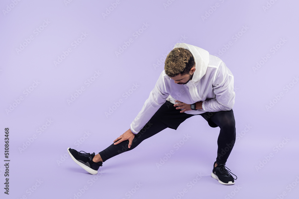 full length of african american sportsman in sportswear doing lunges on purple.