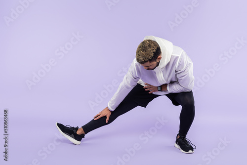 full length of african american sportsman in sportswear doing lunges on purple.
