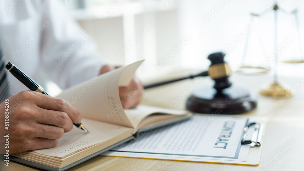 Fototapeta premium Law consultancy concept A male prosecutor reviewing his sentences of contract on his own notebook before writing them down on the contract paper.