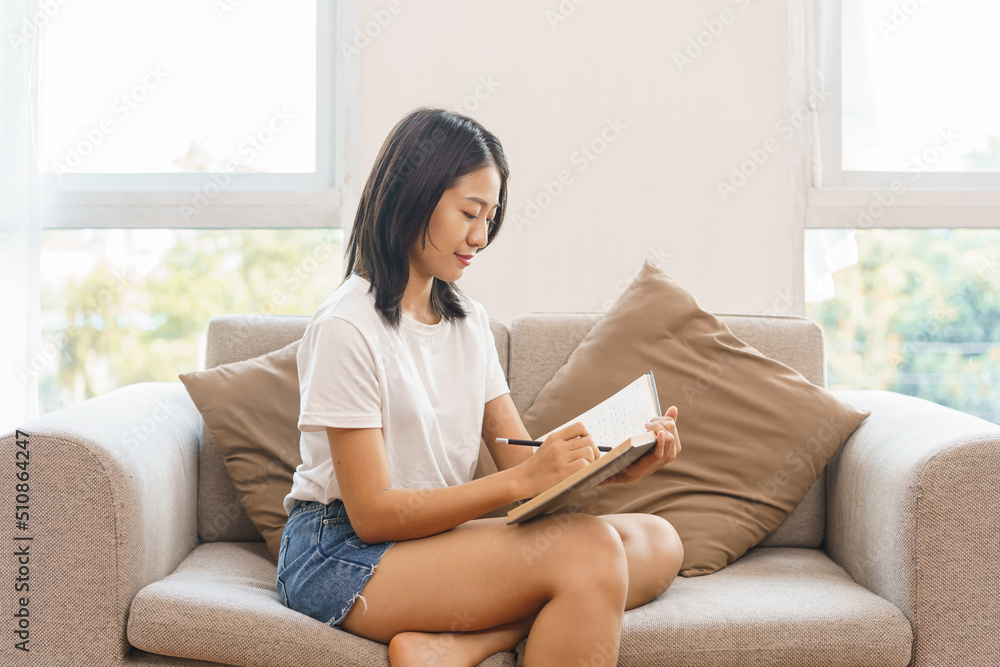 Home relaxation concept, Young woman sitting on couch to taking notes on notebook at home Home relaxation concept, Young woman sitting on couch to taking notes on notebook at home