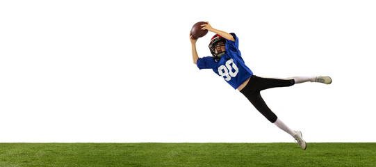 Sportive little boy in sports uniform and equipment playing american football isolated on white background with green grass flooring. Concept of sport, movement, achievements.